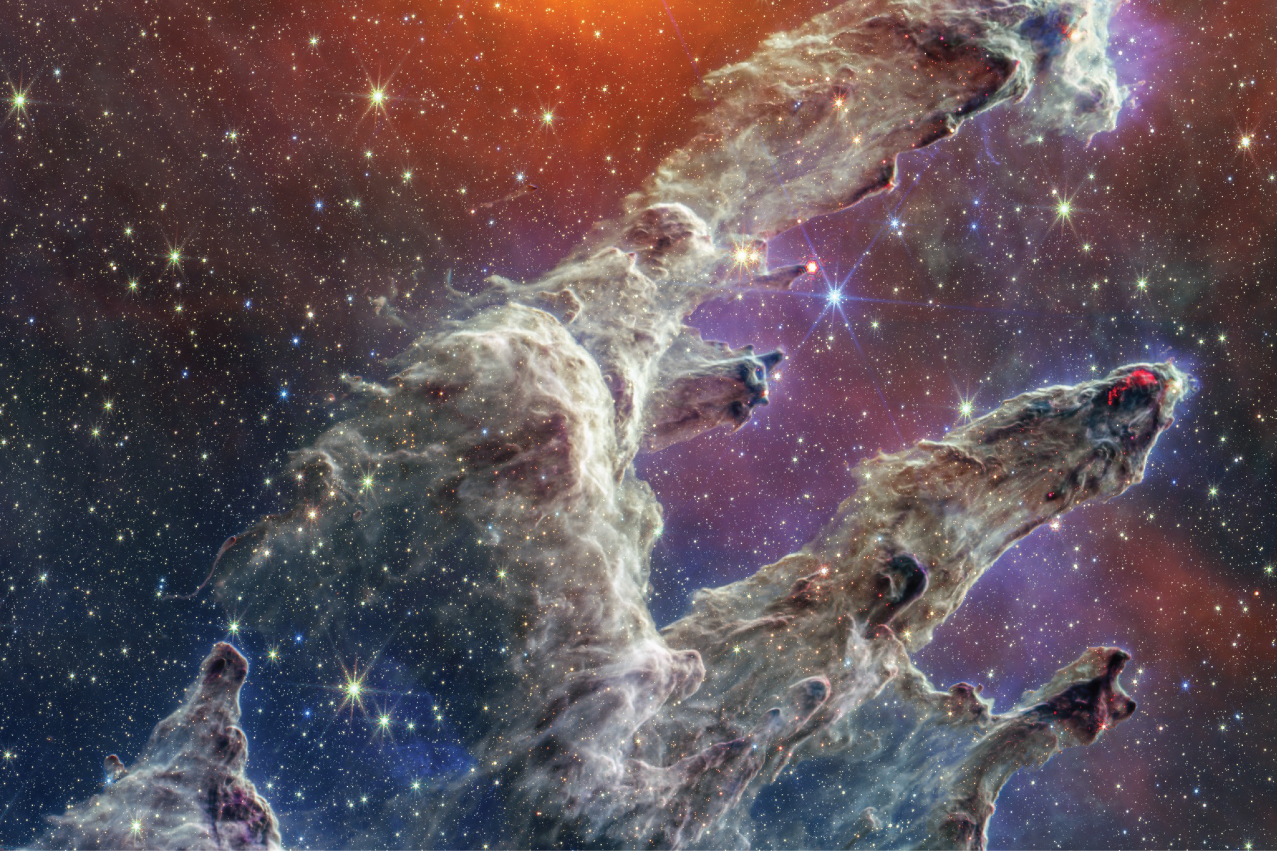 A famous star nebula called pillars of creation. The image has layers of semi-opaque rusty red colored gas and dust that starts at the bottom left and goes toward the top right. There are three prominent pillars rising toward the top right. The left pillar is the largest and widest. The peaks of the second and third pillars are set off in darker shades of brown and have red outlines.
